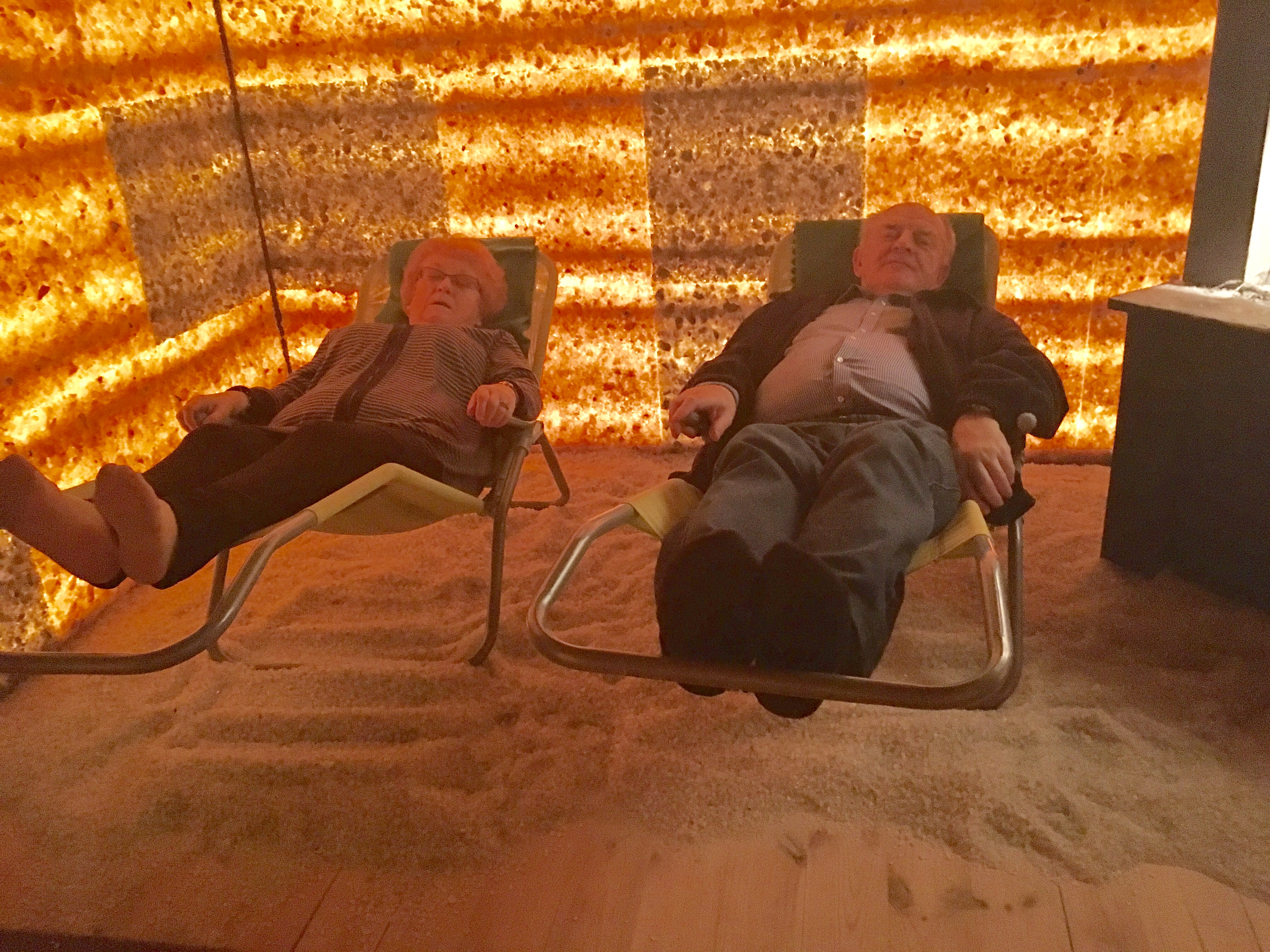 W grocie solnej – dwaj panowie relaksujący się na leżakach w grocie solnej. Pomieszczenie bez okien , ściany podświetlane w brązowo-rudej kolorystyce.