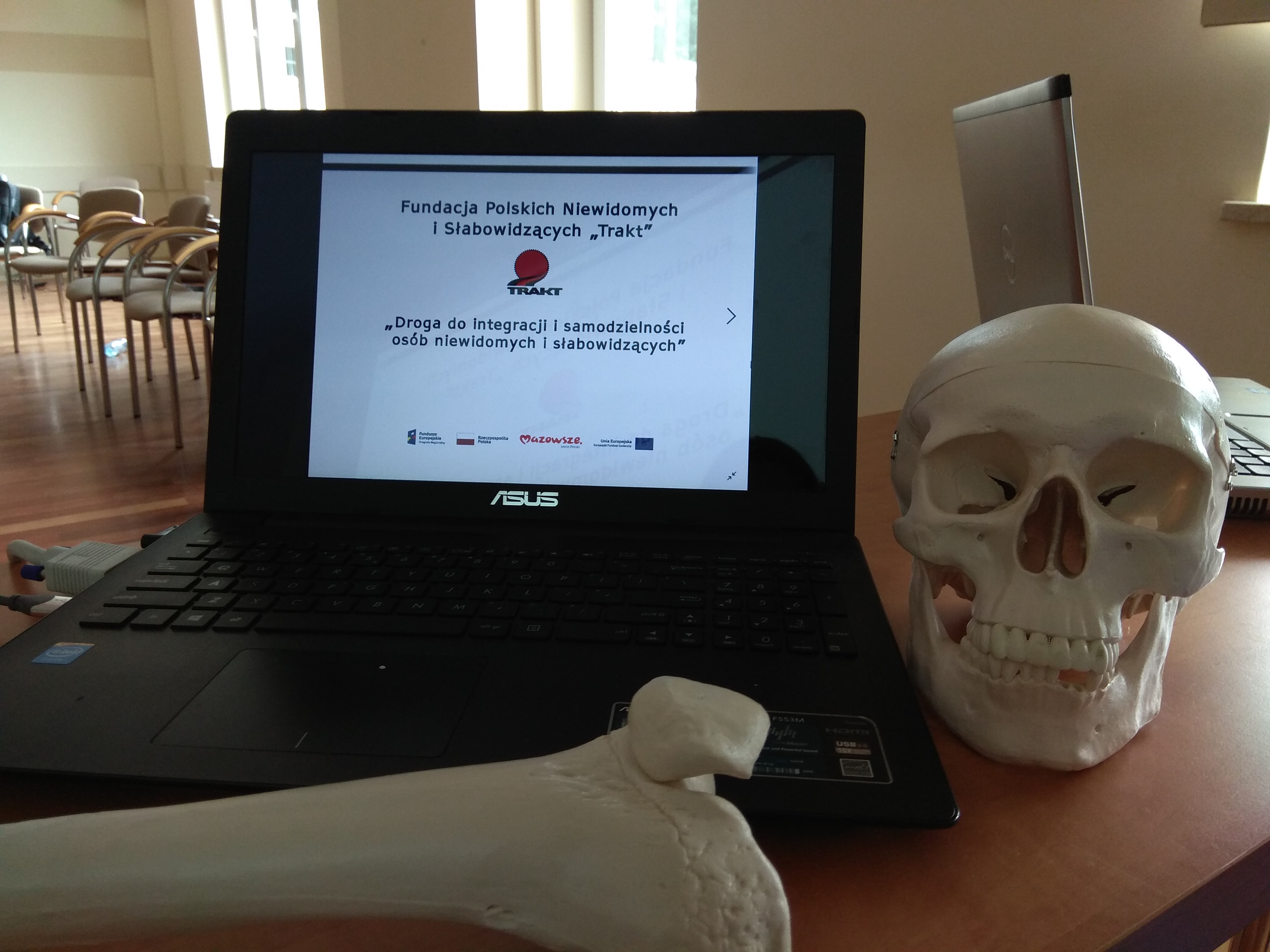 Zbliżenie na laptop z wyświetlonym na ekranie logo fundacji, a obok niego z prawej strony widoczny model czaszki.