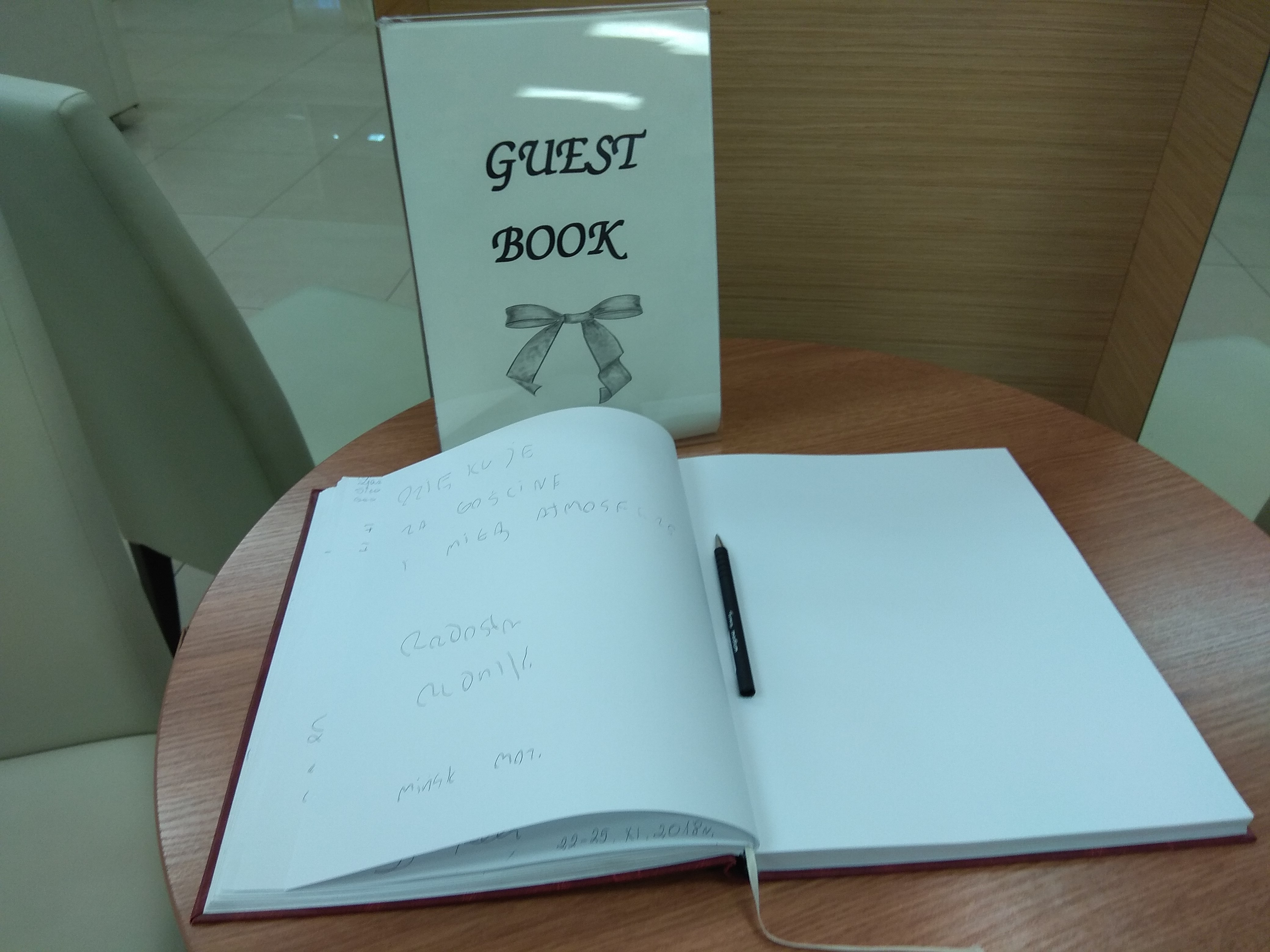 Biała rozłożona księga z czarnym długopisem, a przy niej stojąca tablica z napisem Guest Book.