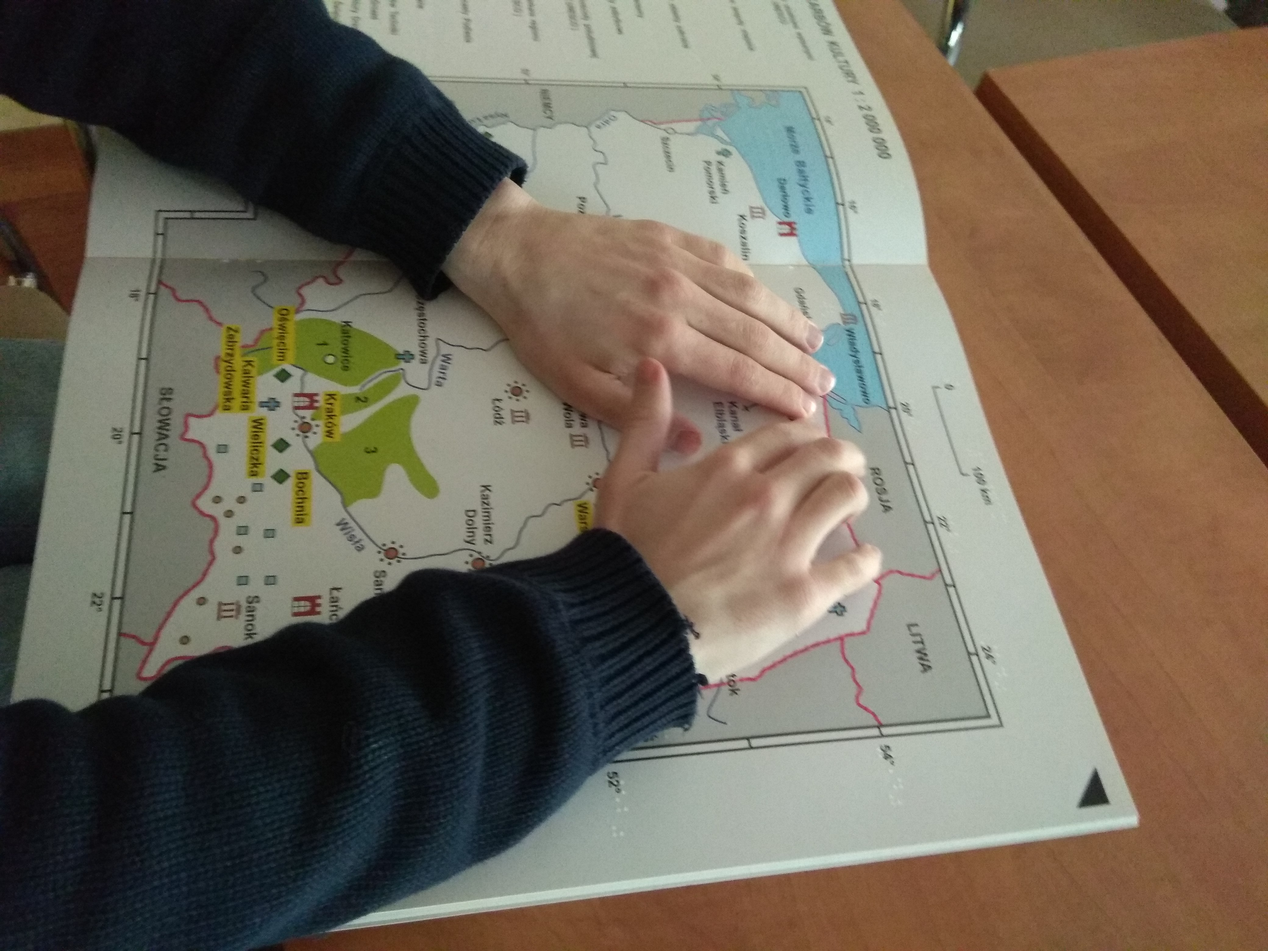 Dłonie uczestnika w czarnych rękawach podczas czytania dotykiem tyflomapy Polski z publikacji Bliżej Skarbów Kultury